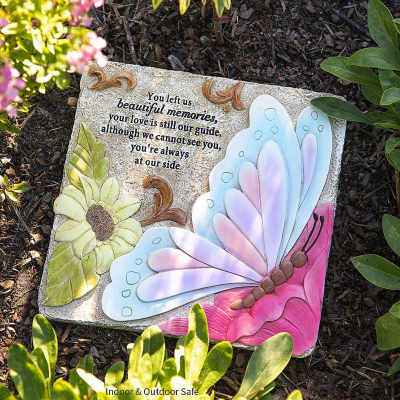 Decorative memorial stone with a butterfly and flower design in a garden bed