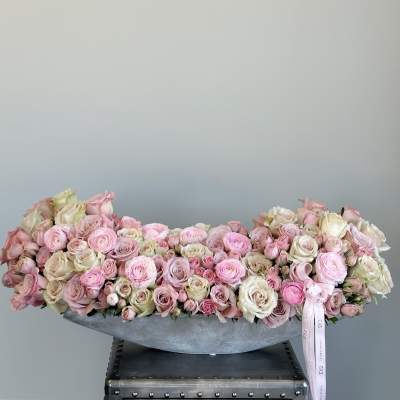 Low arrangement of pink and cream roses in a gray container