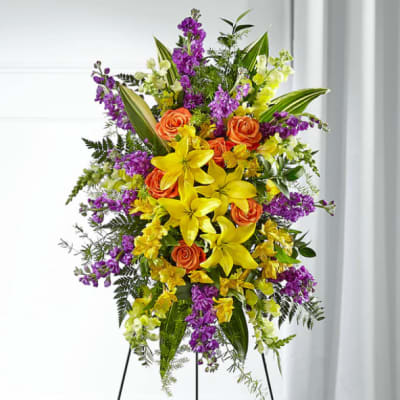 Tall standing floral spray with yellow lilies, orange roses, and purple flowers