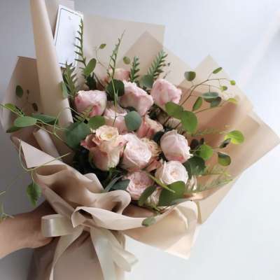 Hand-tied bouquet of pale pink roses wrapped in beige paper