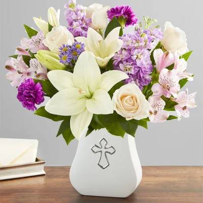 White lilies, roses, and purple flowers in a white vase with a cross