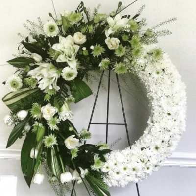 White floral wreath on a black stand with mixed blooms and greenery