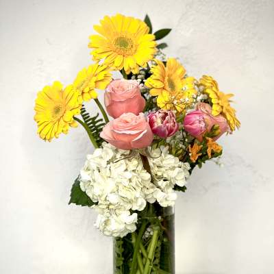 Bouquet of yellow gerbera daisies, pink roses, and white hydrangea in a glass vase