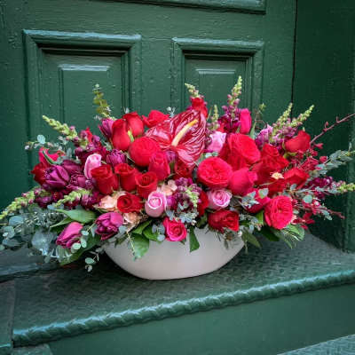 Low floral arrangement of red and pink roses in a white bowl vase