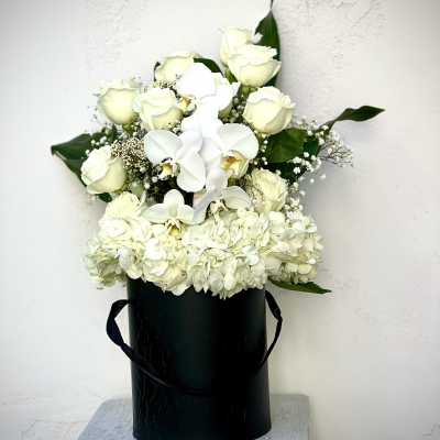 White roses and orchids in a black hatbox with hydrangeas