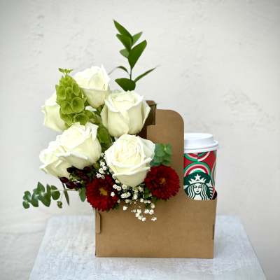 White roses with red flowers in a brown gift box beside a Starbucks cup
