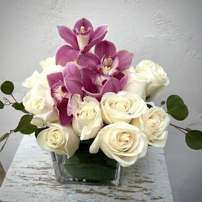 White roses with pink orchids in a square glass vase