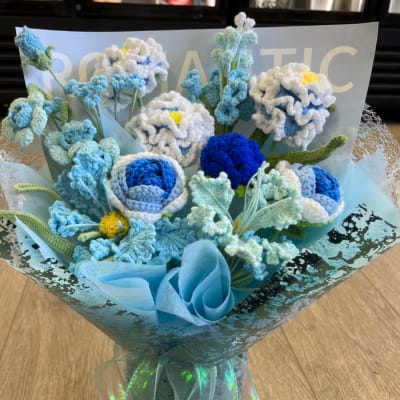 Bouquet of blue and white crocheted flowers wrapped in shimmering blue paper and ribbon