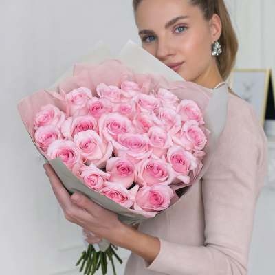 Woman holding a large bouquet of pink roses wrapped in pale paper