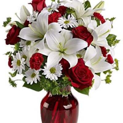 Arrangement of white lilies, red roses, red carnations, and white daisies in a red glass vase