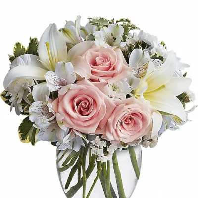 Compact bouquet of pale pink roses and white lilies in a clear glass vase