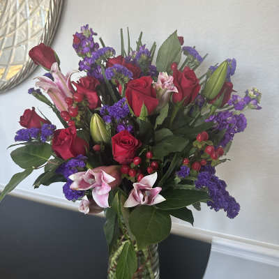 Bouquet of red roses, pink lilies, and purple flowers in a clear glass vase