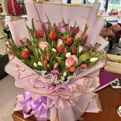 Bouquet of pink, purple, and orange tulips with roses wrapped in pink paper