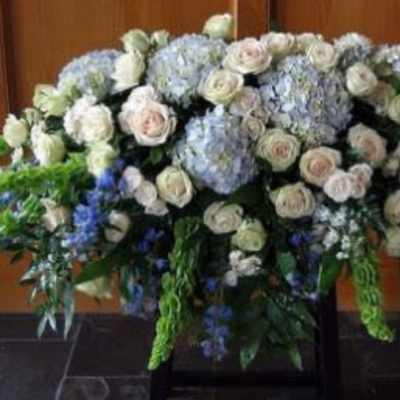 Large white rose and blue hydrangea spray with Bells of Ireland arranged on a stand