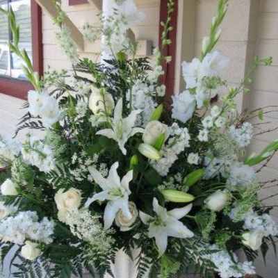 Tall all-white arrangement with lilies, roses, and snapdragons in a white pedestal vase
