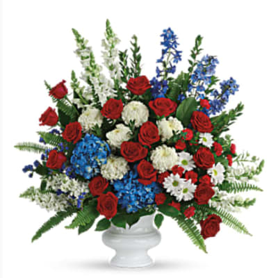Large red, white, and blue flower arrangement in a white pedestal urn