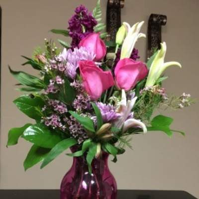Pink and white mixed flower arrangement with roses and lilies in a bright pink glass vase