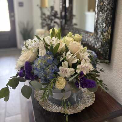 Mixed bouquet in a low silver bowl with cream, blue, and purple flowers