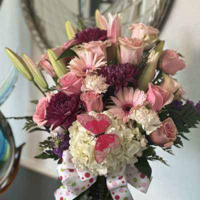 Tall pink and white mixed flower arrangement in a glass vase with ribbon and butterfly decoration