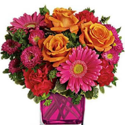 Bright arrangement of orange roses and hot pink gerbera daisies in a pink glass cube vase