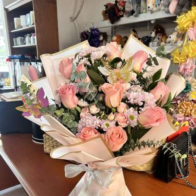 Pink rose bouquet with small daisies wrapped in pale paper and a silver bow