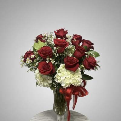 Red roses and white hydrangeas in a clear glass vase with a red ribbon