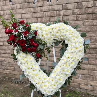 Heart-shaped floral wreath with white chrysanthemums and red roses on a stand