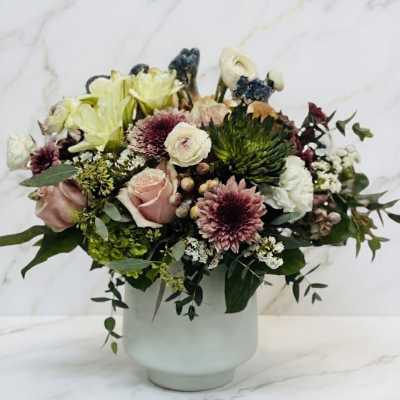 Muted pink and cream flower arrangement with roses, mums, and lilies in a white ceramic vase
