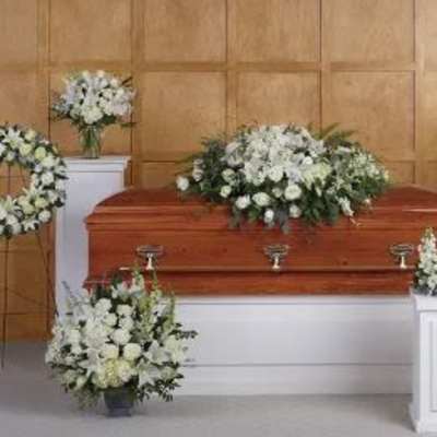 Set of white funeral flower arrangements surrounding a wooden casket in a chapel setting