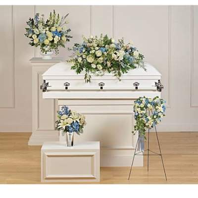 Funeral floral set with white and blue arrangements on a white casket, pedestals, vase, and standing heart wreath.