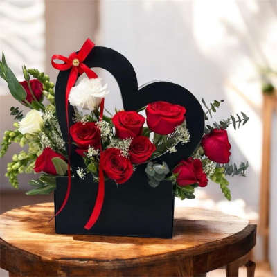 Red and white roses arranged in a black heart-shaped box with a red ribbon