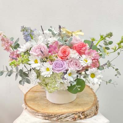Pastel bouquet of roses and daisies in a white container