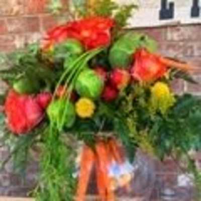 Arrangement of mixed red and green blooms with carrots in a round glass bowl vase