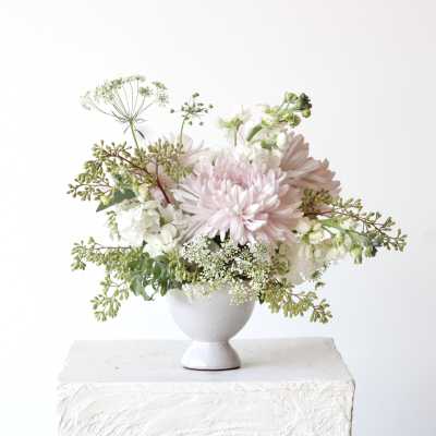 Soft pink and white flowers arranged in a white pedestal vase
