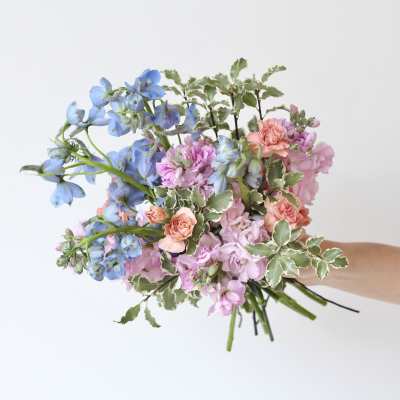 Handheld bouquet of blue and pink flowers with variegated foliage