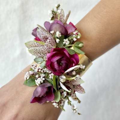 Purple floral wrist corsage with small white blossoms and green leaves