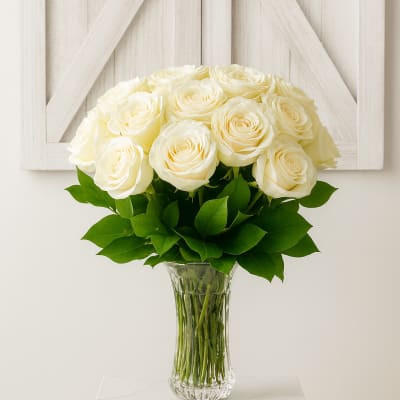 White roses arranged in a clear glass vase with green leaves