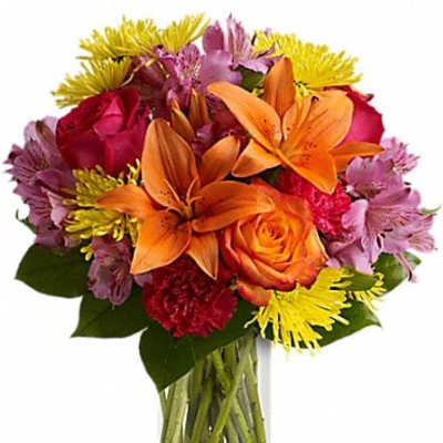 Mixed bouquet of orange lilies, roses, and colorful daisies in a glass vase