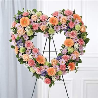 Heart-shaped floral wreath on a stand with pink, peach, orange, and lavender blooms
