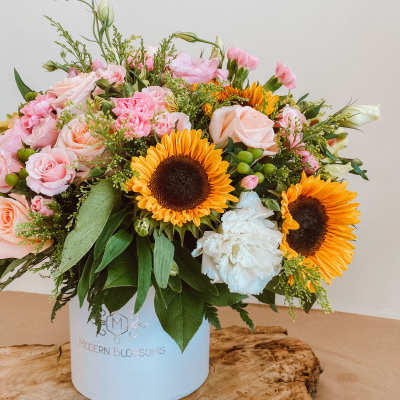 Mixed bouquet of pink roses, sunflowers, and white blooms in a blue box