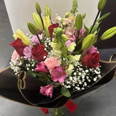 Bouquet of red roses, lilies, and pink flowers wrapped in black paper