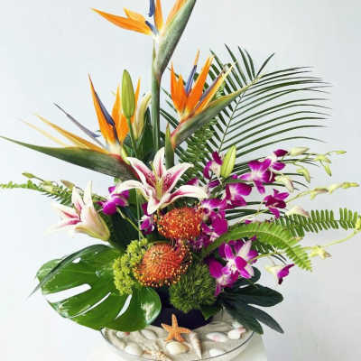Tropical flower arrangement with orange bird-of-paradise and purple orchids in a low container