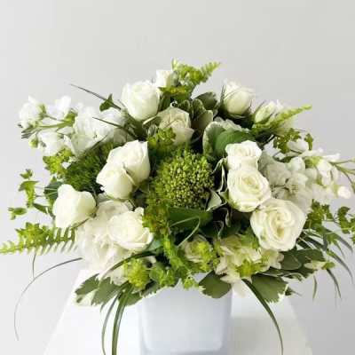 White rose arrangement in a white square vase with green accents
