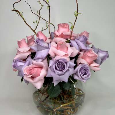 Pink and lavender roses arranged in a round glass vase with curly branches