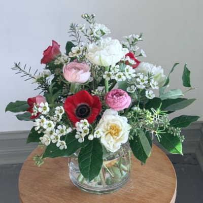 Mixed arrangement of red, pink, and white flowers in a clear glass vase on a wooden table