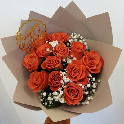 Orange roses with baby's breath in tan wrapping and a "happy birthday" topper