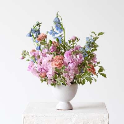 Pink and blue mixed flower arrangement in a white pedestal vase