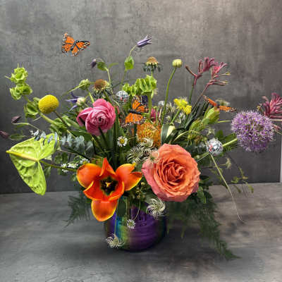 Colorful mixed flower arrangement in a purple vase with butterfly picks