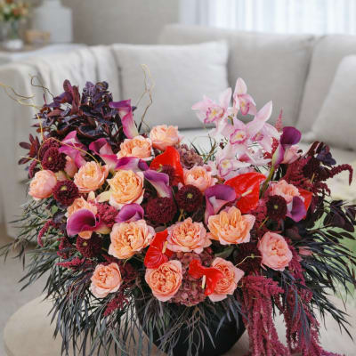 Large mixed floral arrangement with peach roses, pink orchids, and red anthuriums in a black vase