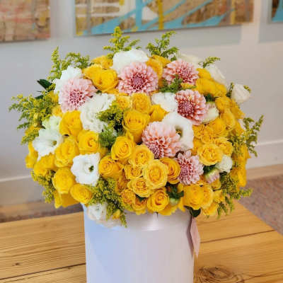Yellow, white, and blush flowers arranged in a white hat box
